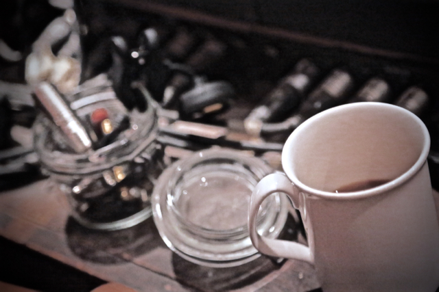 half-empty coffee cup next to an out-of-focus jar of music gear doodads