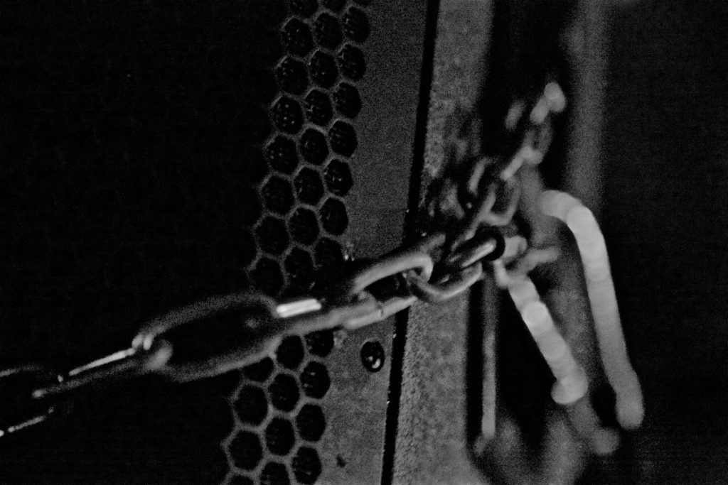 Close-up black and white photo of a speaker wrapped in mounting chains