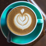 overhead photo of a turquoise coffee cup with hearts made out of latte foam