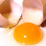 photo of a cracked-open egg with the empty shells sitting behind it