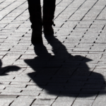 Black-and-white photo of two people's legs and their shadows on a brick sidewalk