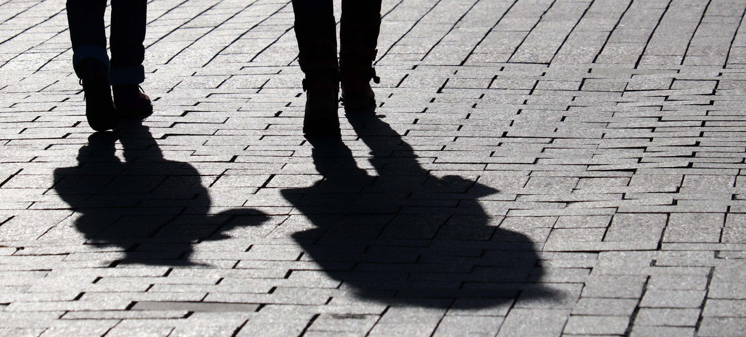 Black-and-white photo of two people's legs and their shadows on a brick sidewalk