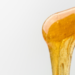 close-up photo of a wooden stick with golden hair removal wax dripping from it