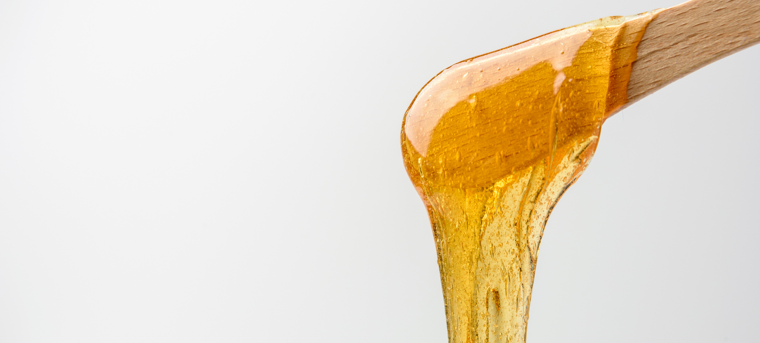 close-up photo of a wooden stick with golden hair removal wax dripping from it