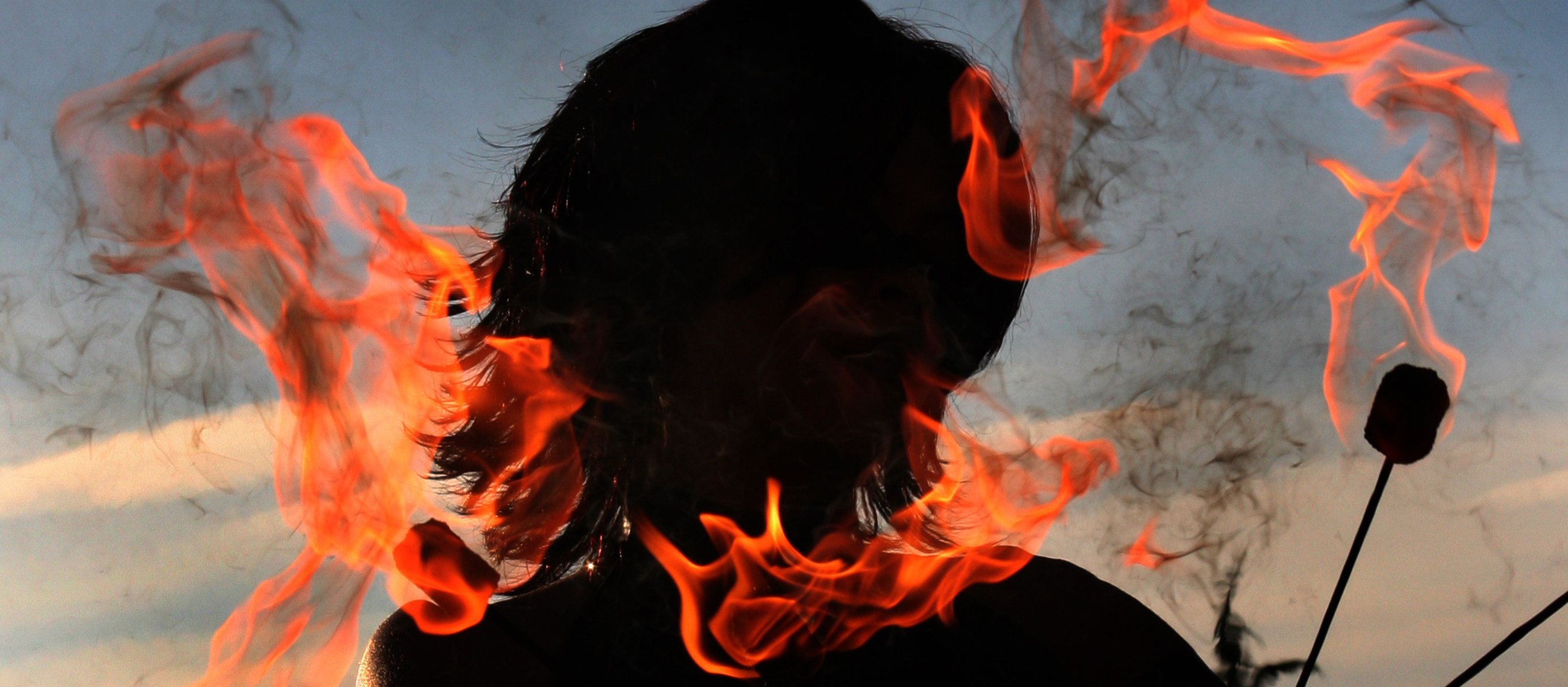 Photo of a woman's silhouette holding lit fire-eating sticks