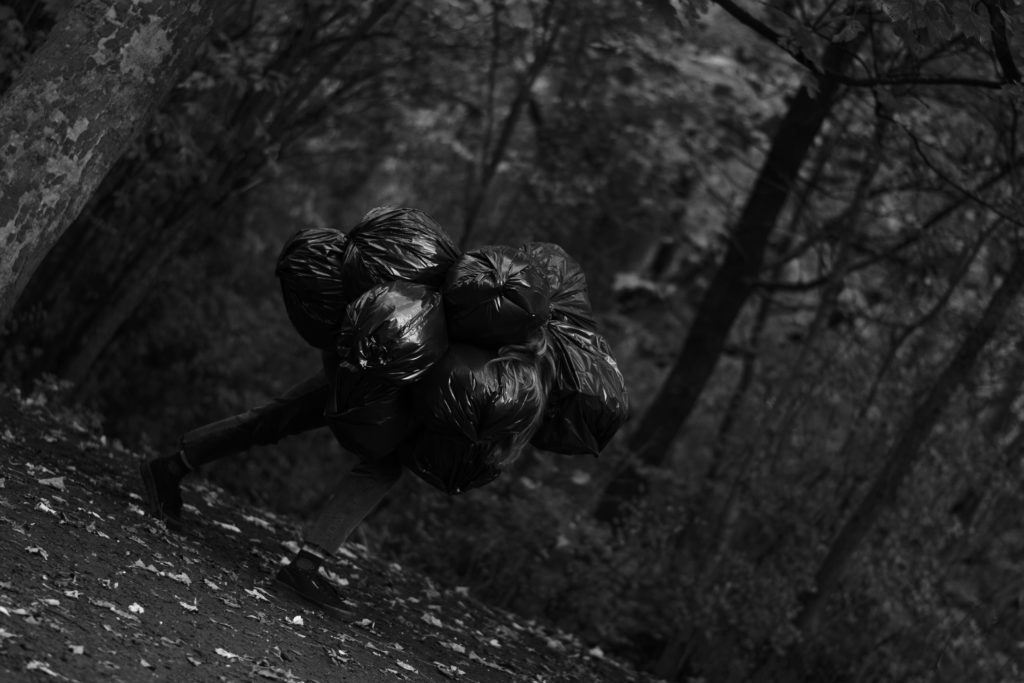 Woman in the woods carrying a large group of black trash bags on her back