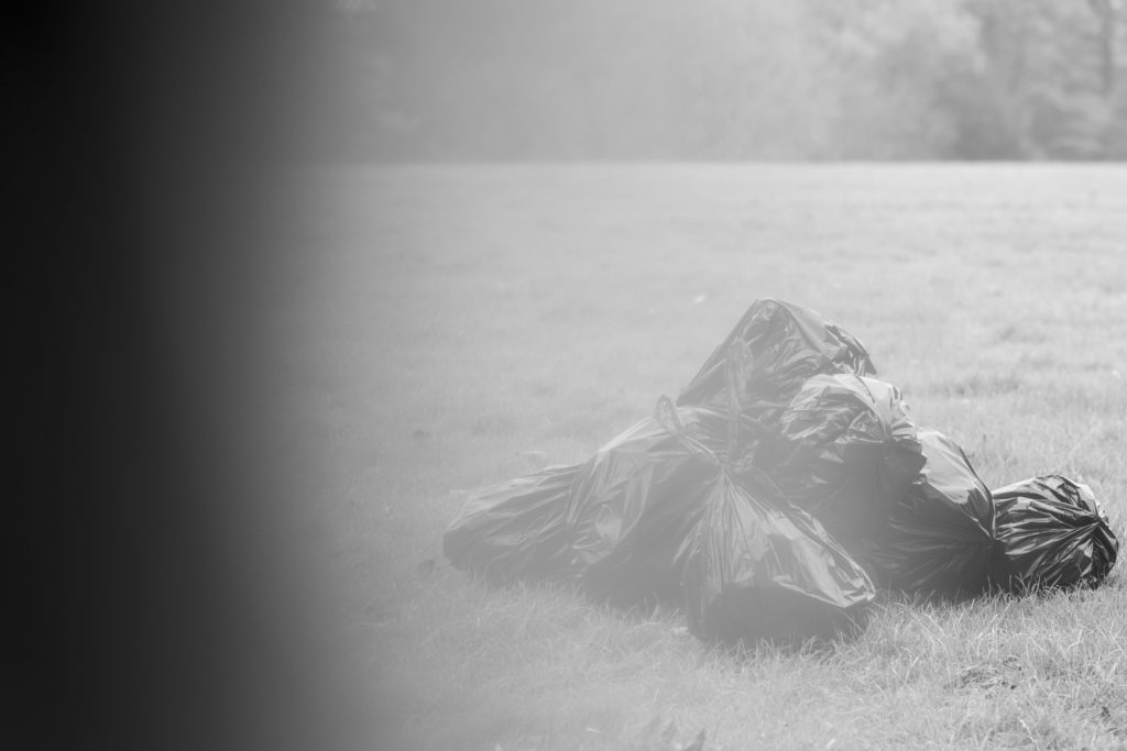 Semi-obscured photo of a pile of black trash bags sitting in a field