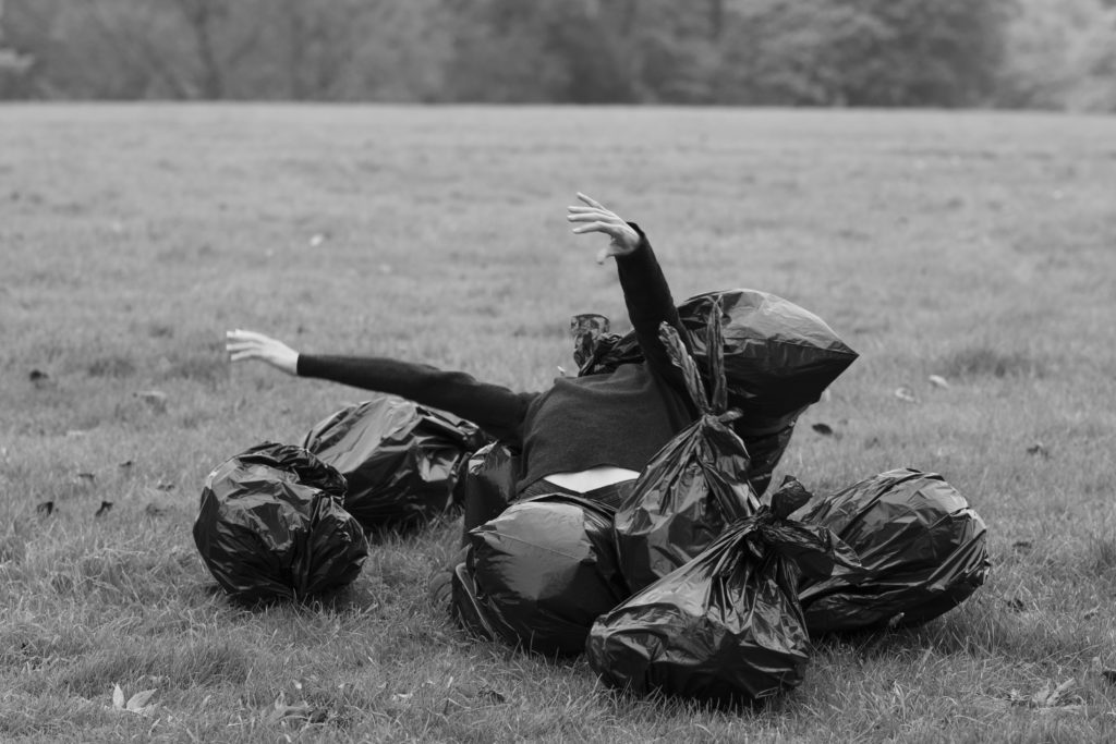 Photo of woman breaking out of a pile of black trash bags in the middle of a field