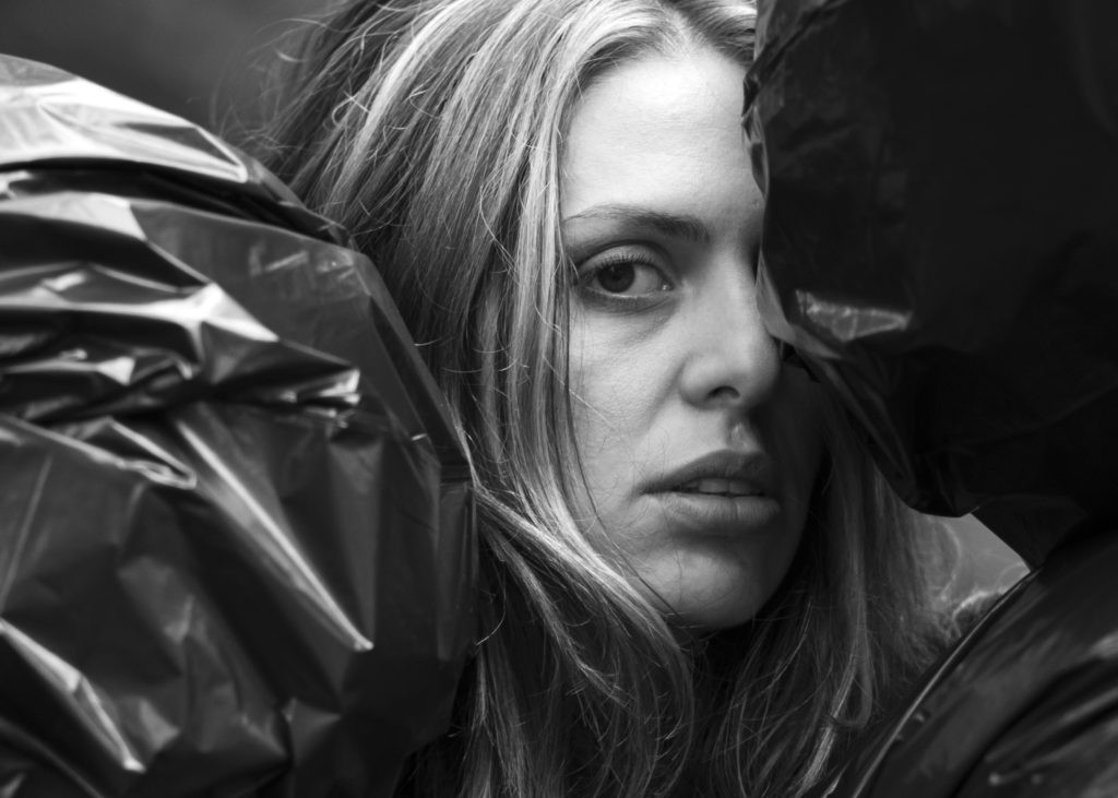 Close-up photo of a woman's face in half profile with black garbage bags nearly obscuring her