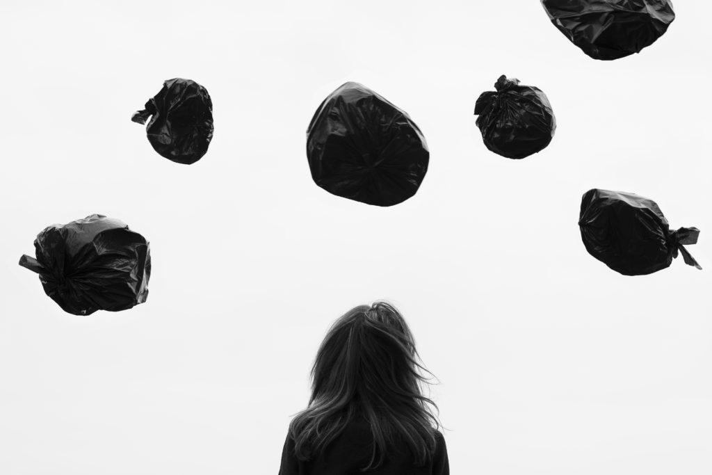 Woman staring at several black trash bags up in the air