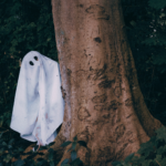 Photo of a person in a ghost costume hiding behind a tree