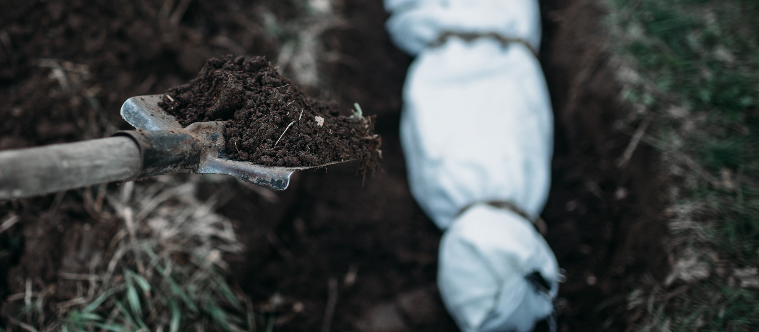 Photo of a shovel dropping dirt on a covered dead body