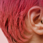 Close-up photo of the side of a woman's head and ear. Her hair is cut into a bright pink pixie cut.